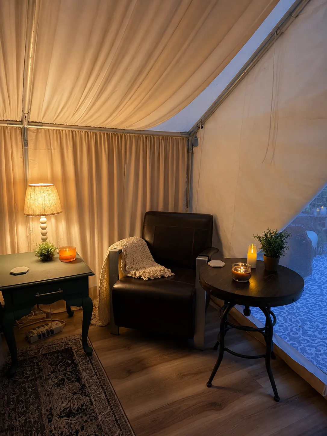 A leather lounge chair inside The Velvet Buck with a knit throw over the arm, a lit table lamp and candles on the side tables, and the deck visible through the canvas doorway.